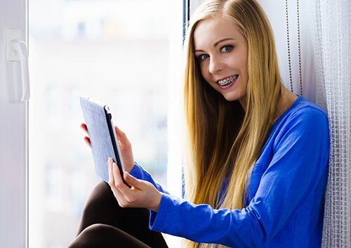 Student girl with tablet sitting on windowsill